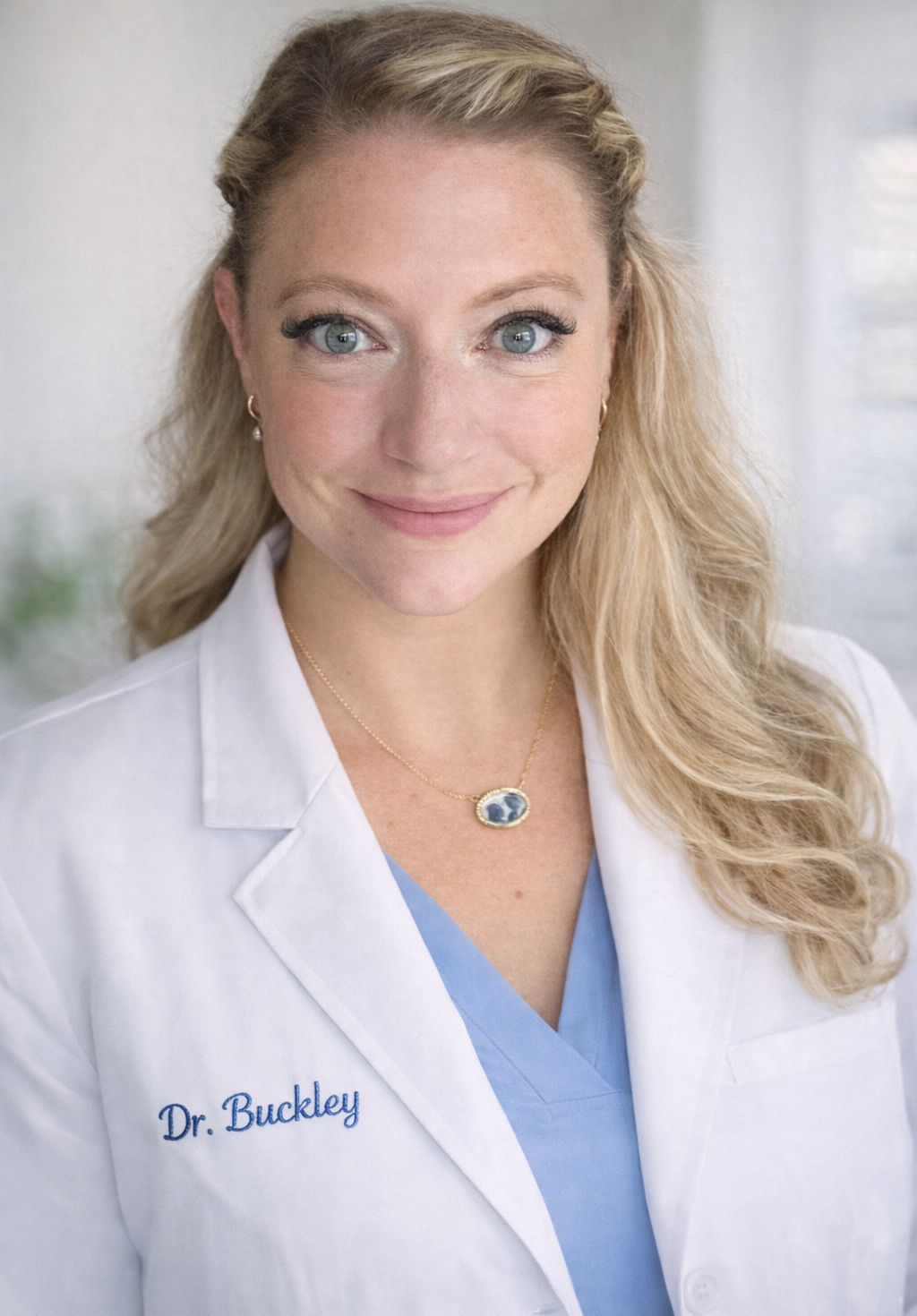 Blonde woman smiling, wearing a black blazer and pink shirt, against a gray background.