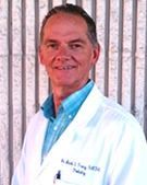 Dr. Bob Furg, MD, smiling in a white coat, standing outdoors near a striped wall.