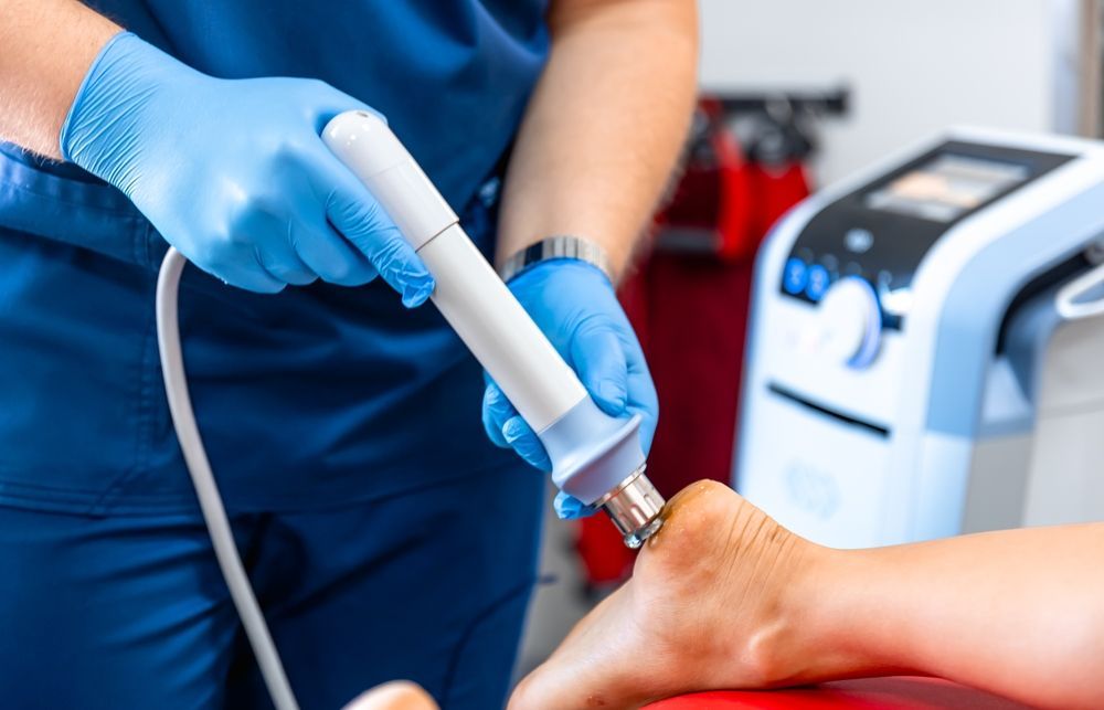 A medical professional in blue gloves uses shockwave therapy on a patient's foot.