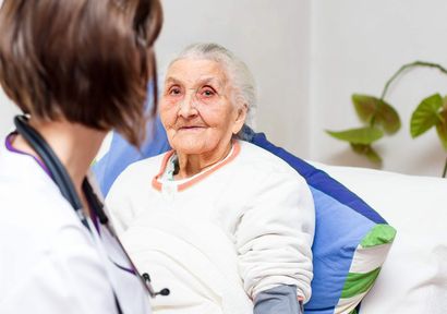 An elderly woman is sitting on a couch talking to a doctor.
