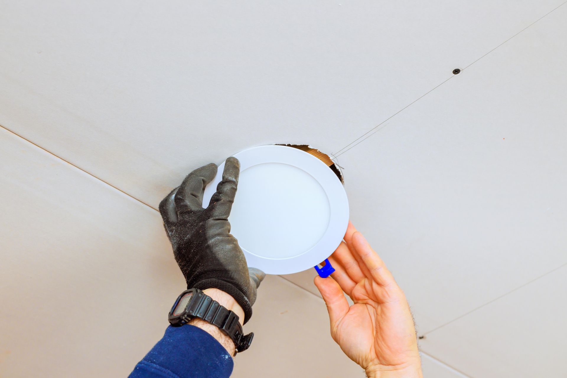 Des mains installent un plafonnier rond blanc sur un plafond blanc.