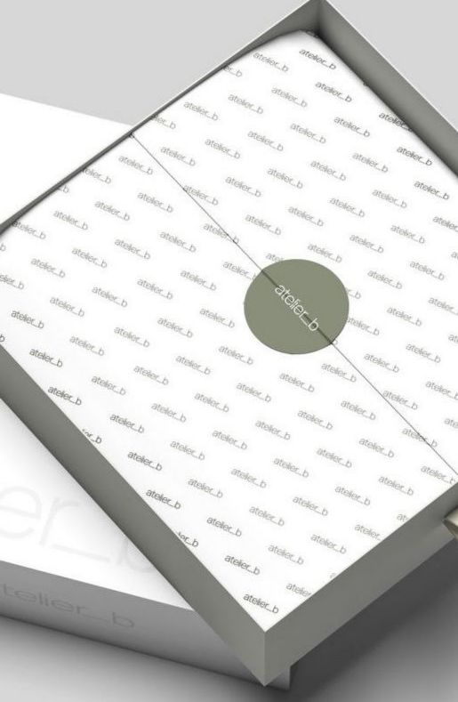 Open white gift box with the lid slightly ajar, showing a white paper pattern and a small, green circular seal.