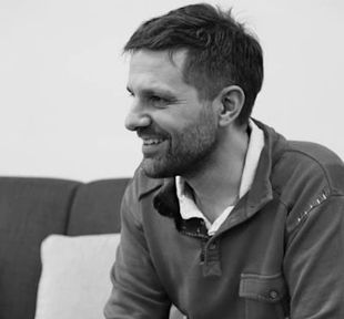 A man with a beard is sitting on a couch and smiling.