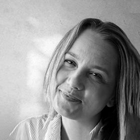 A black and white photo of a woman smiling in front of a window.