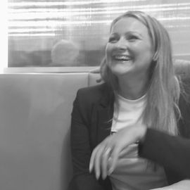 A woman is sitting on a couch and smiling in a black and white photo.