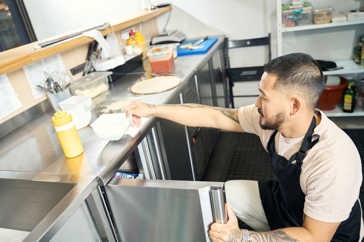 Person cleaning a kitchen counter beside a sink and yellow bottle in a bright commercial kitchen