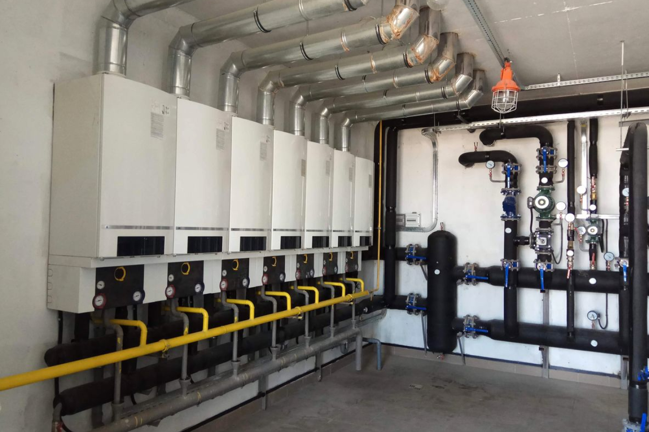 Industrial boiler room with white wall-mounted units, black piping, and yellow gas lines.
