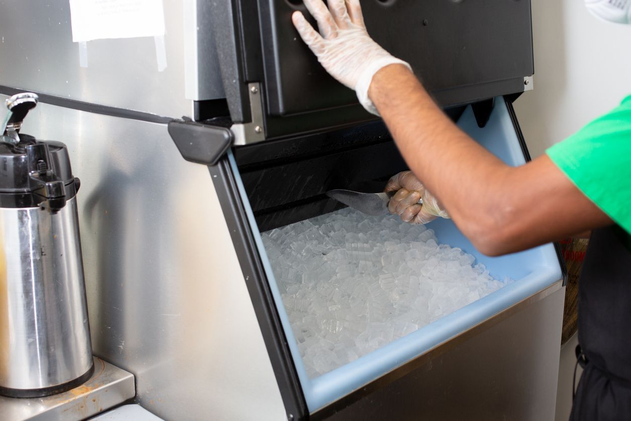 Worker refilling ice machine with gloved hand in a stainless steel kitchen setting