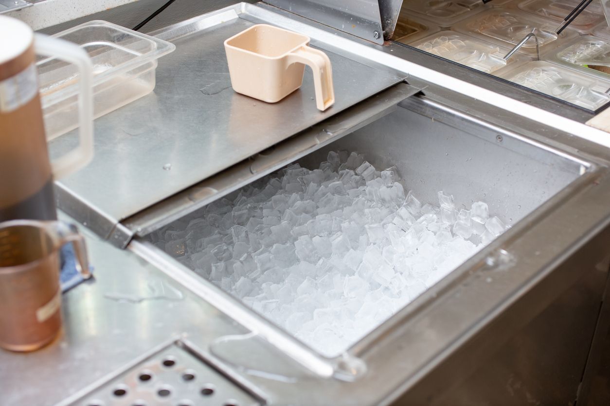 Ice-filled metal sink with a beige scoop on a countertop, likely in a kitchen or bar area