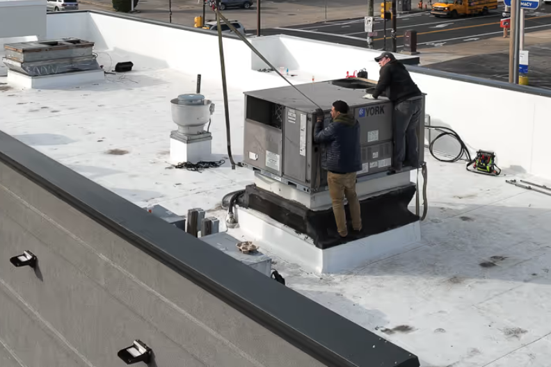 Two workers servicing rooftop HVAC unit on a flat white roof