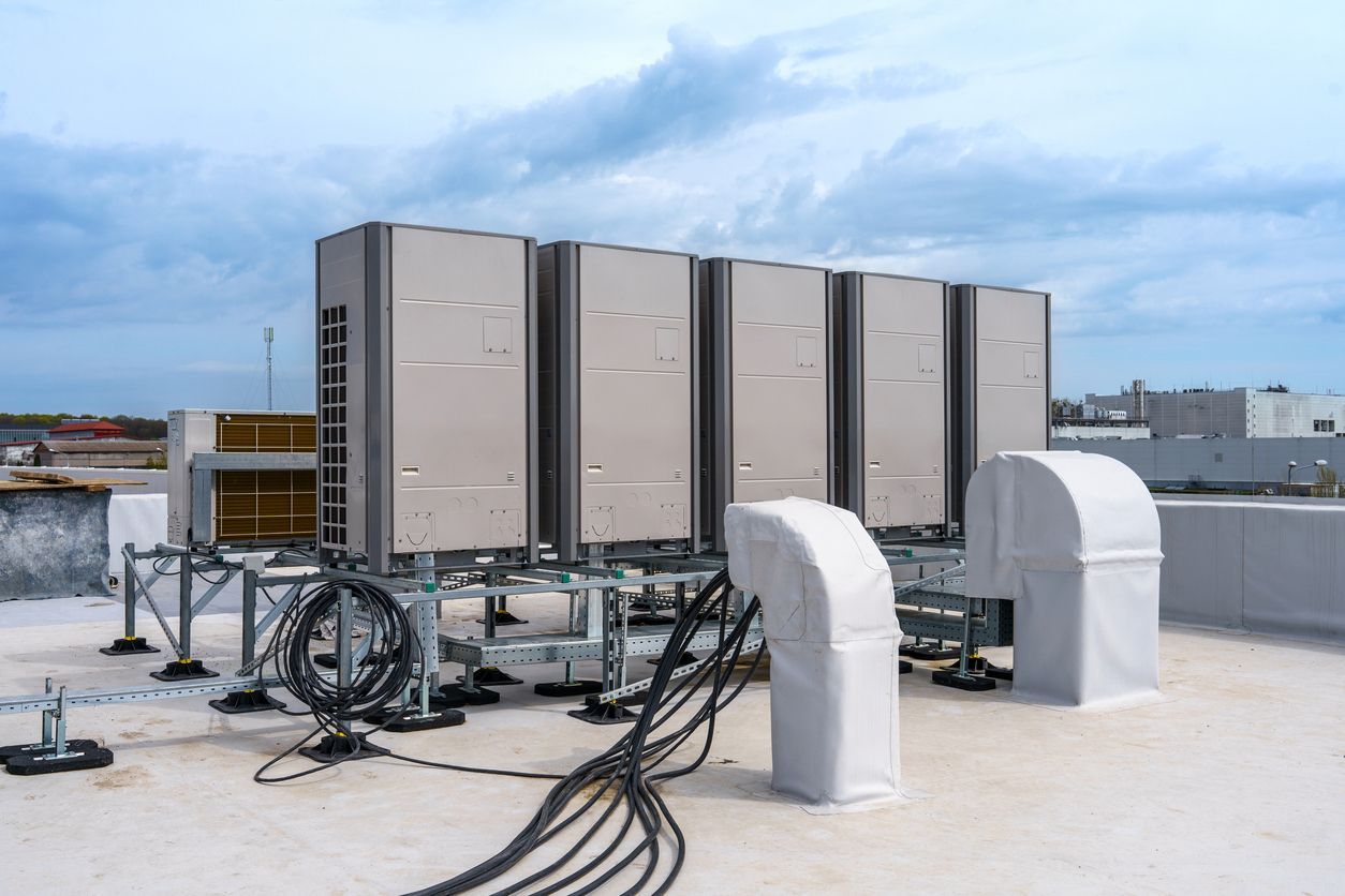 Rooftop HVAC units and black cables on a white building under a cloudy sky