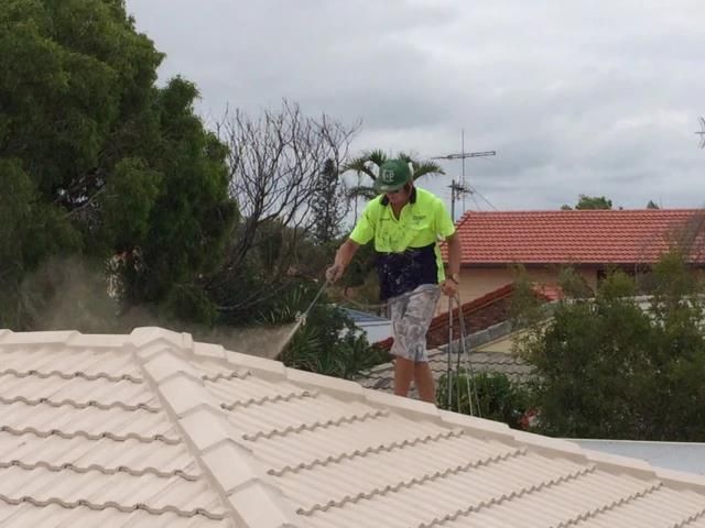 A Man is Standing on Top of a Roof Using a High Pressure Washer — Roofing Revamped in Maroochydore, QLD