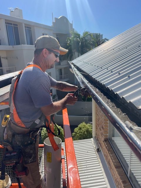 A Man Is Working On A Gutter On A Roof — Roofing Revamped in Maroochydore, QLD