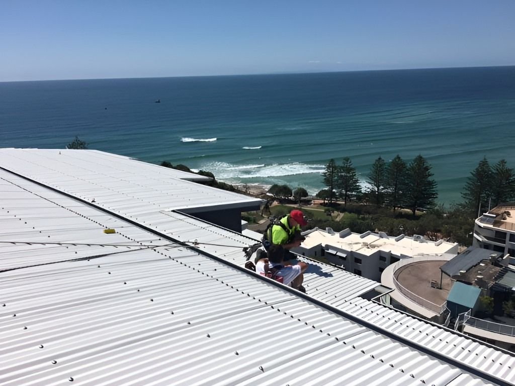 A Man is Standing on the Roof of a Building Overlooking the Ocean — Roofing Revamped in Maroochydore, QLD