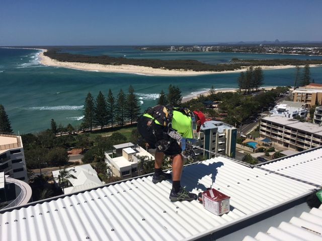 A Man is Fixing the Roof of a Building Overlooking the Ocean — Roofing Revamped in Maroochydore, QLD