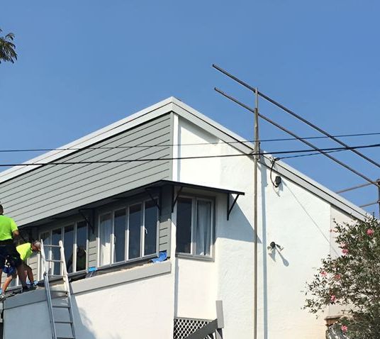 A Man is Standing on a Ladder on the Side of a Building — Roofing Revamped in Wurtulla, QLD