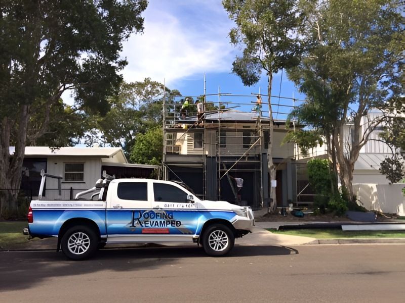 A blue and white truck is parked in front of a house under construction.