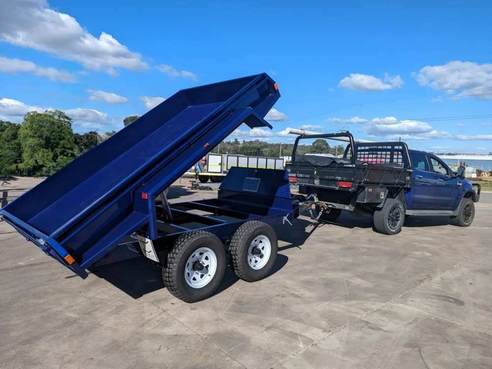A Blue Dump Trailer Is Being Towed By A Truck In A Parking Lot — Eddies Trailers & Fab in Muswellbrook, NSW