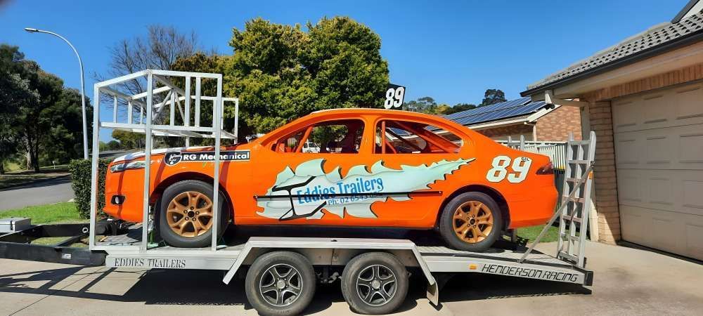 An Orange Race Car Is On A Trailer In Front Of A Garage — Eddies Trailers & Fab in Muswellbrook, NSW