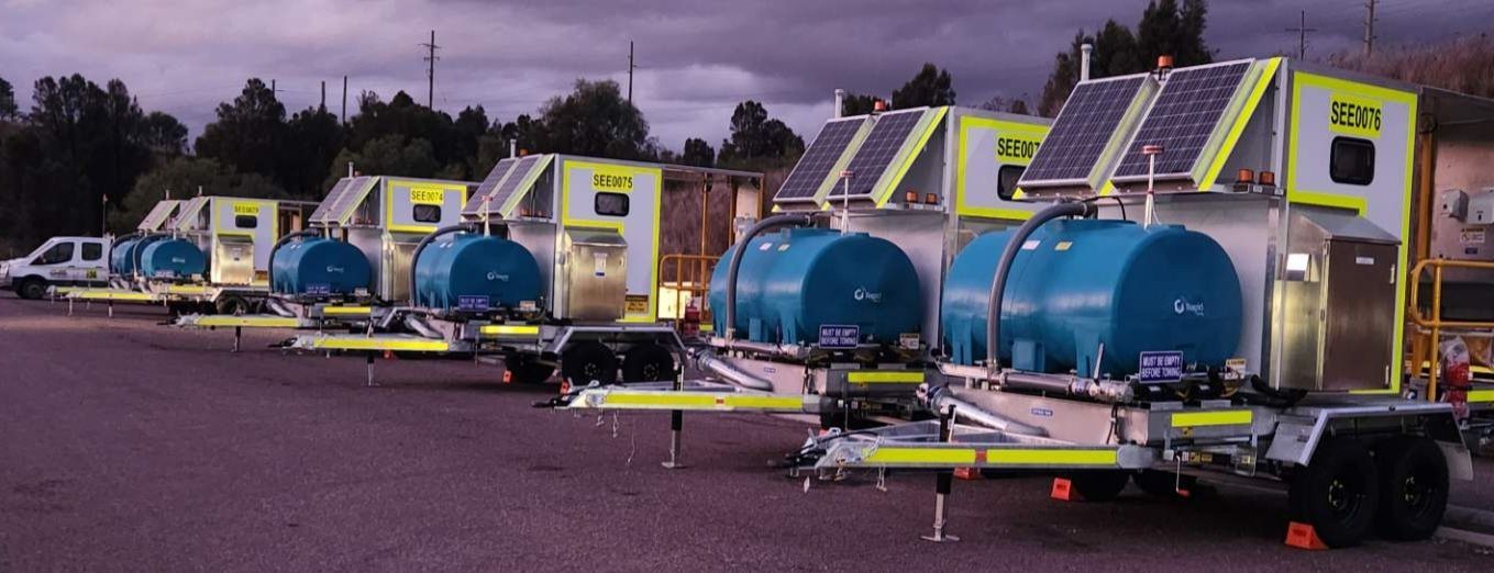 A row of trailers with blue tanks on them are parked in a parking lot.