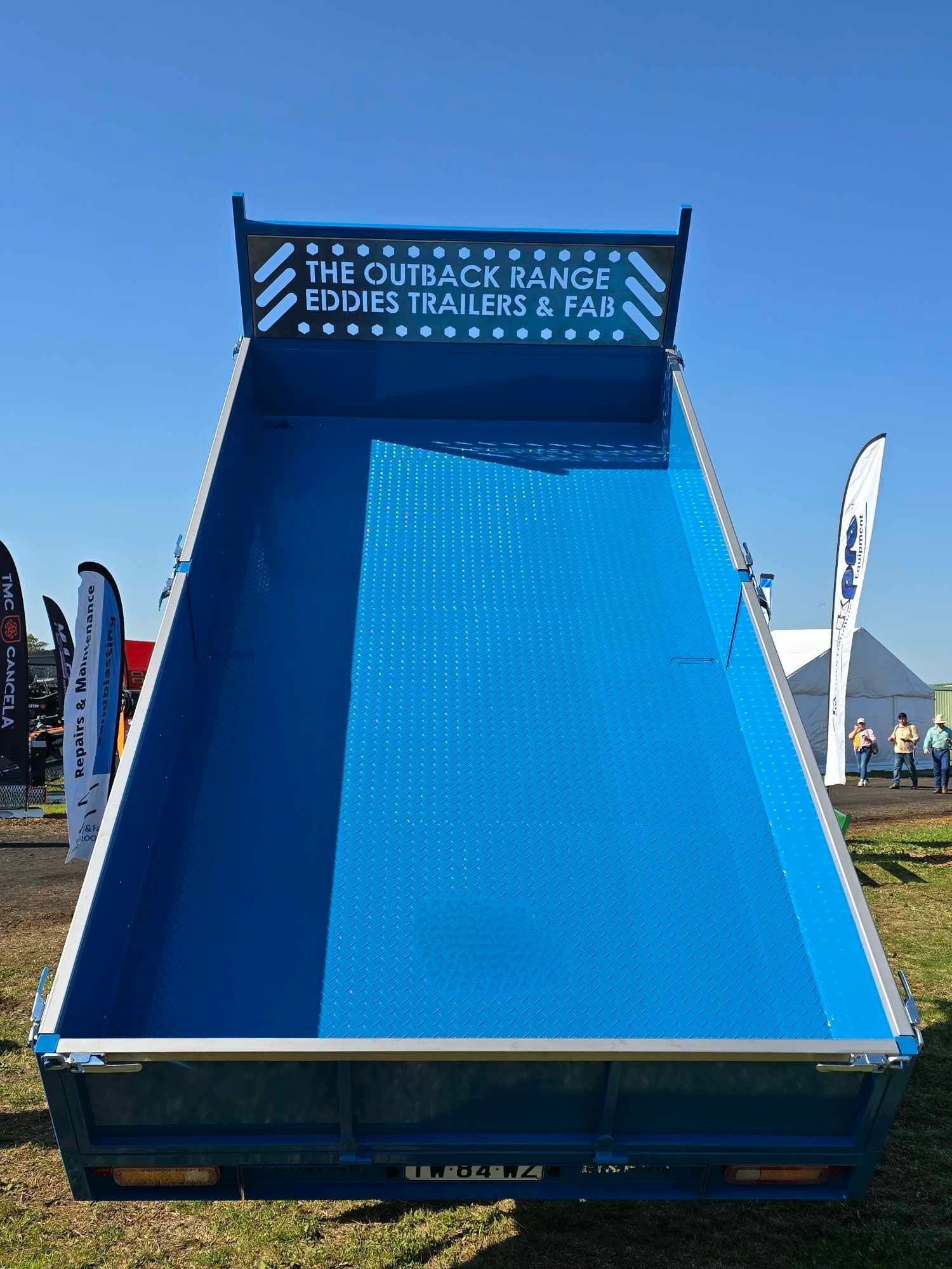 A blue dump truck is parked in a grassy field.