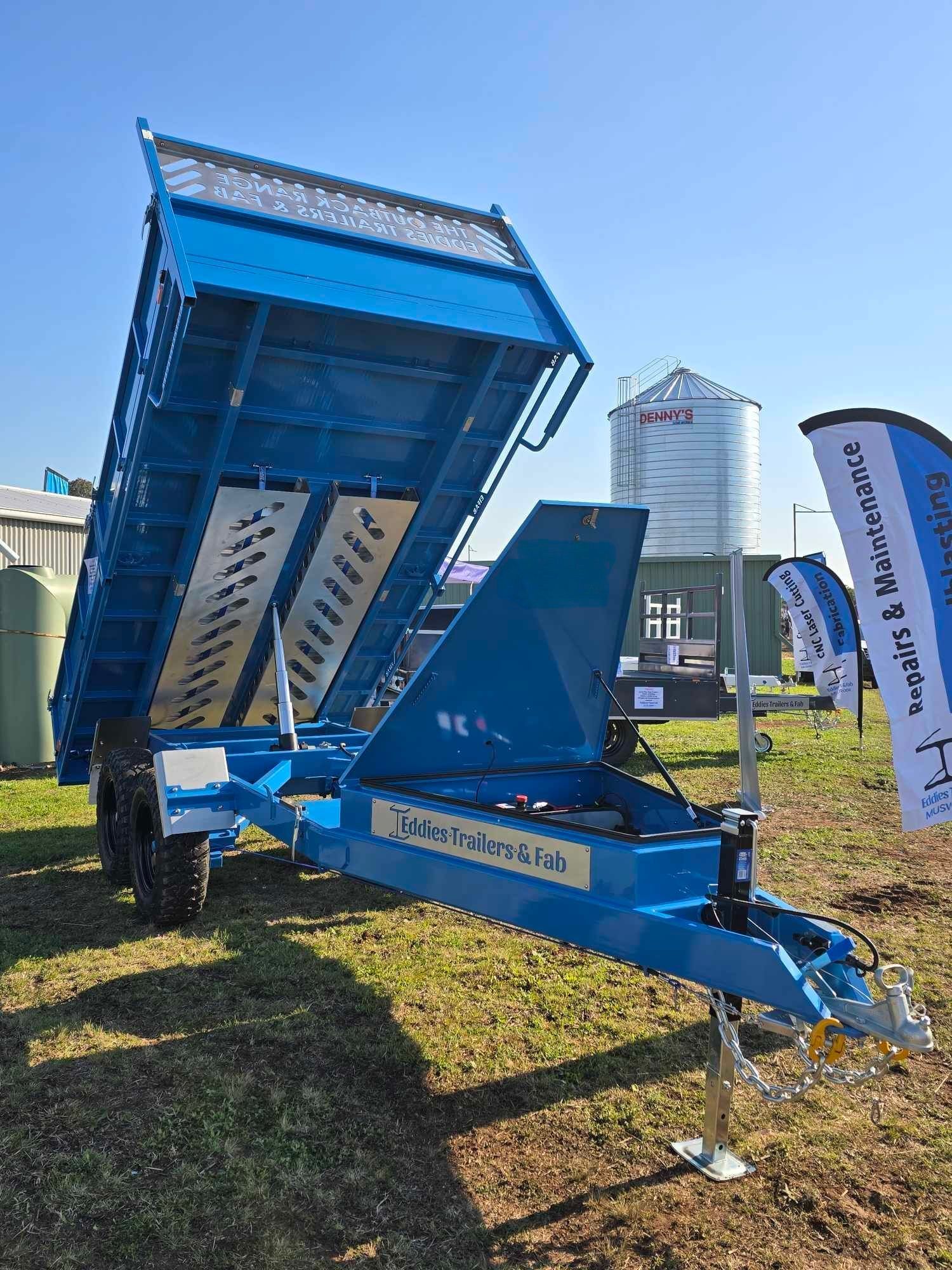 A blue dump trailer is parked in a grassy field.
