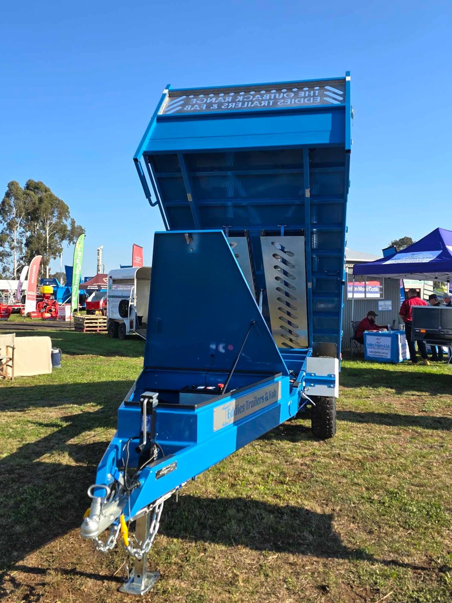A blue dump trailer is parked in a grassy field.