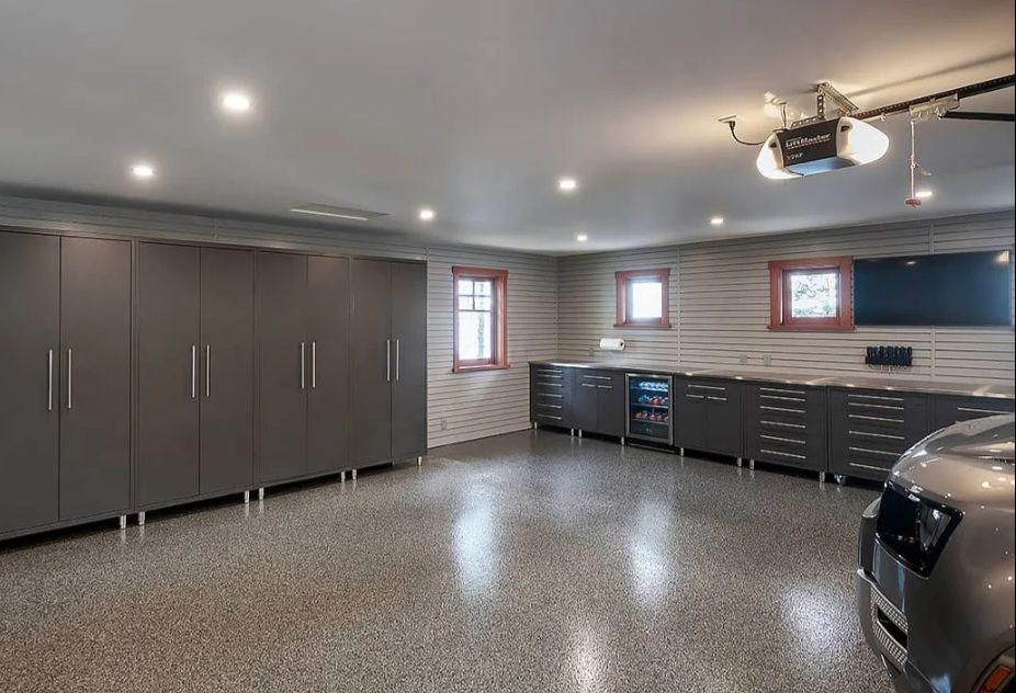 A modern, well-organized garage with gray cabinets, a shiny floor, and a car parked inside.