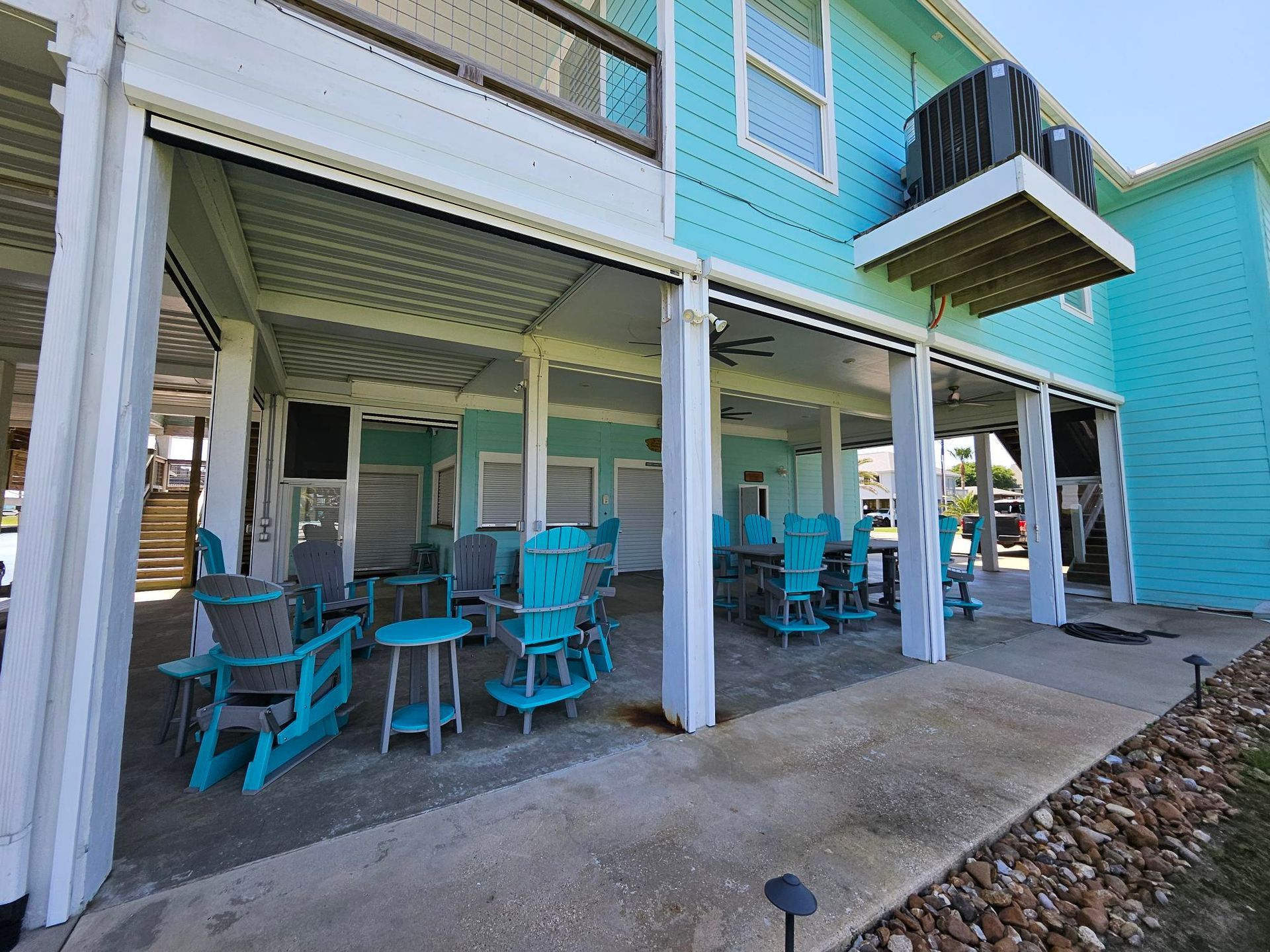 Covered outdoor seating area with turquoise chairs and light blue house.