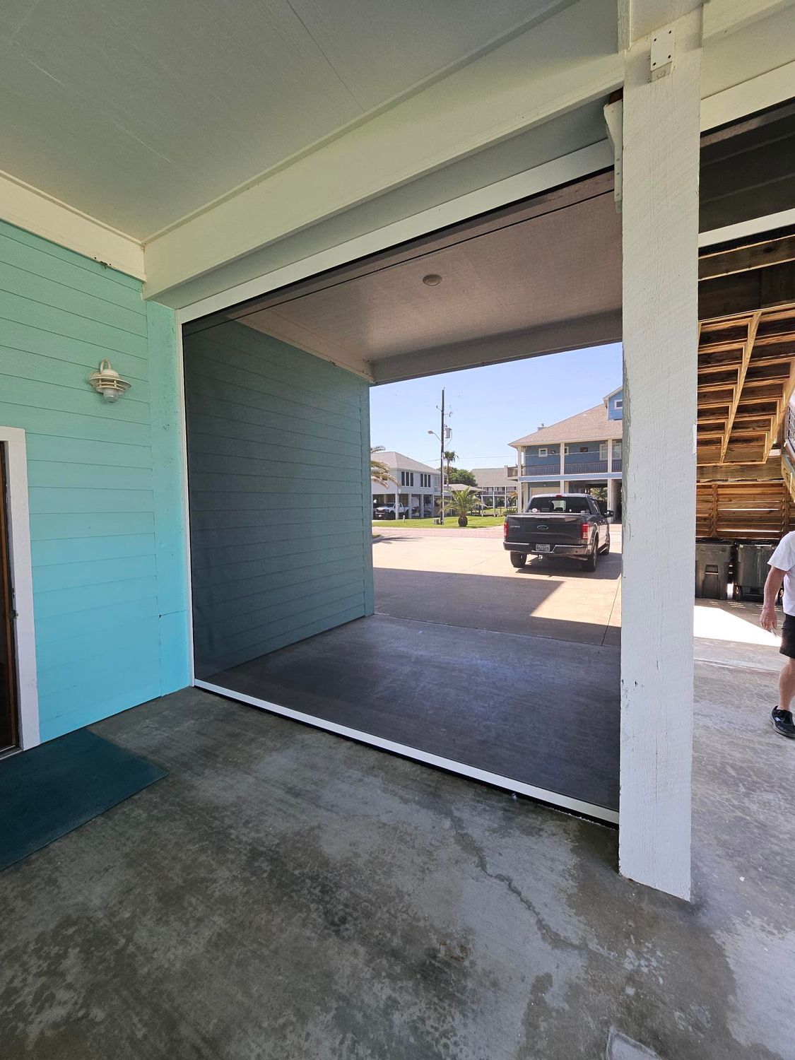 View from a covered entranceway, looking out to a street with parked vehicles. Aqua and white building trim.
