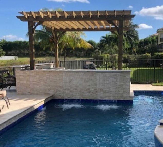 Pergola over a pool with a stone wall and water feature, blue water, sunny day.