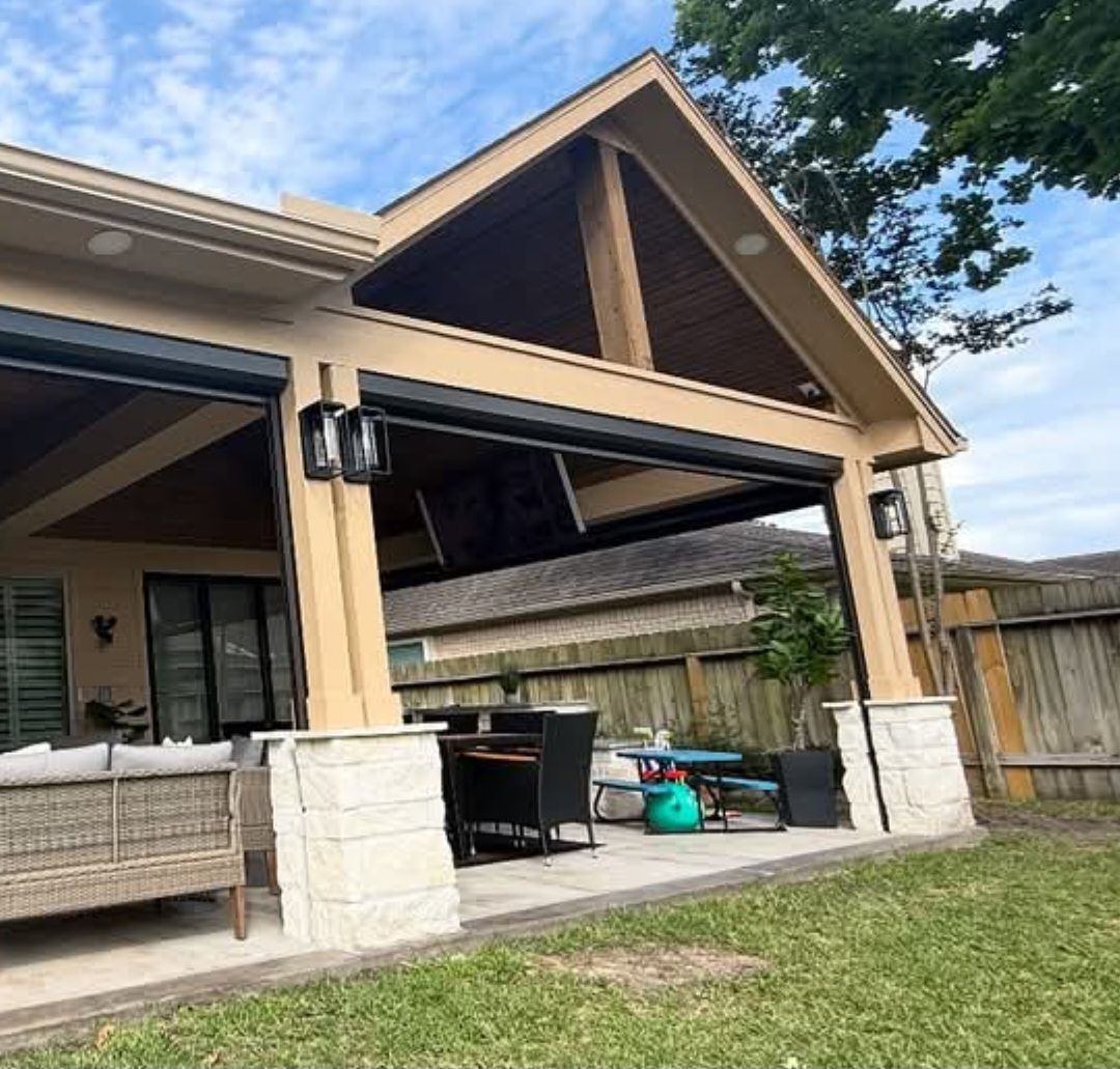 Covered patio with retractable screens, stone columns, furniture, and a grassy backyard.