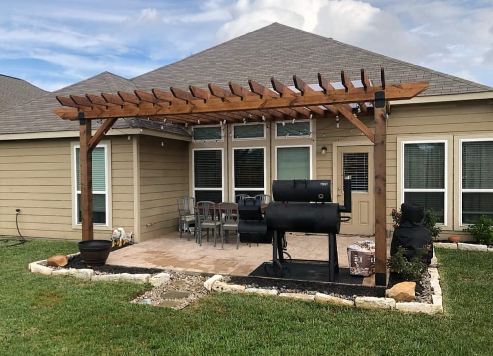 Backyard patio with wooden pergola, smoker, and seating.