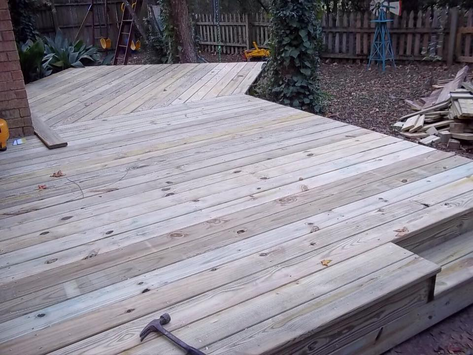 Wooden deck construction with angled design, steps, and hammer, outdoor setting.