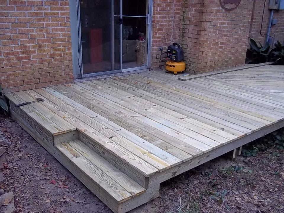 Wooden deck with steps next to a brick building and a sliding glass door.