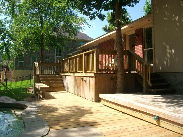 Wooden deck with stairs, a tree, and a two-story house in the background. Sunny day.