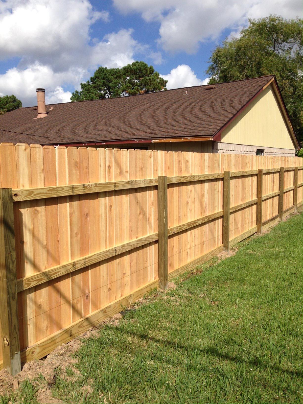 Wooden fence in front of a house, set on green grass under a blue sky.