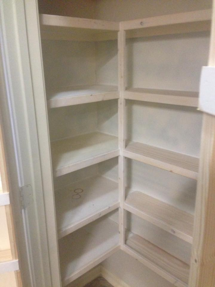 Corner pantry with built-in light wood shelves, painted light tan. Interior of a room.