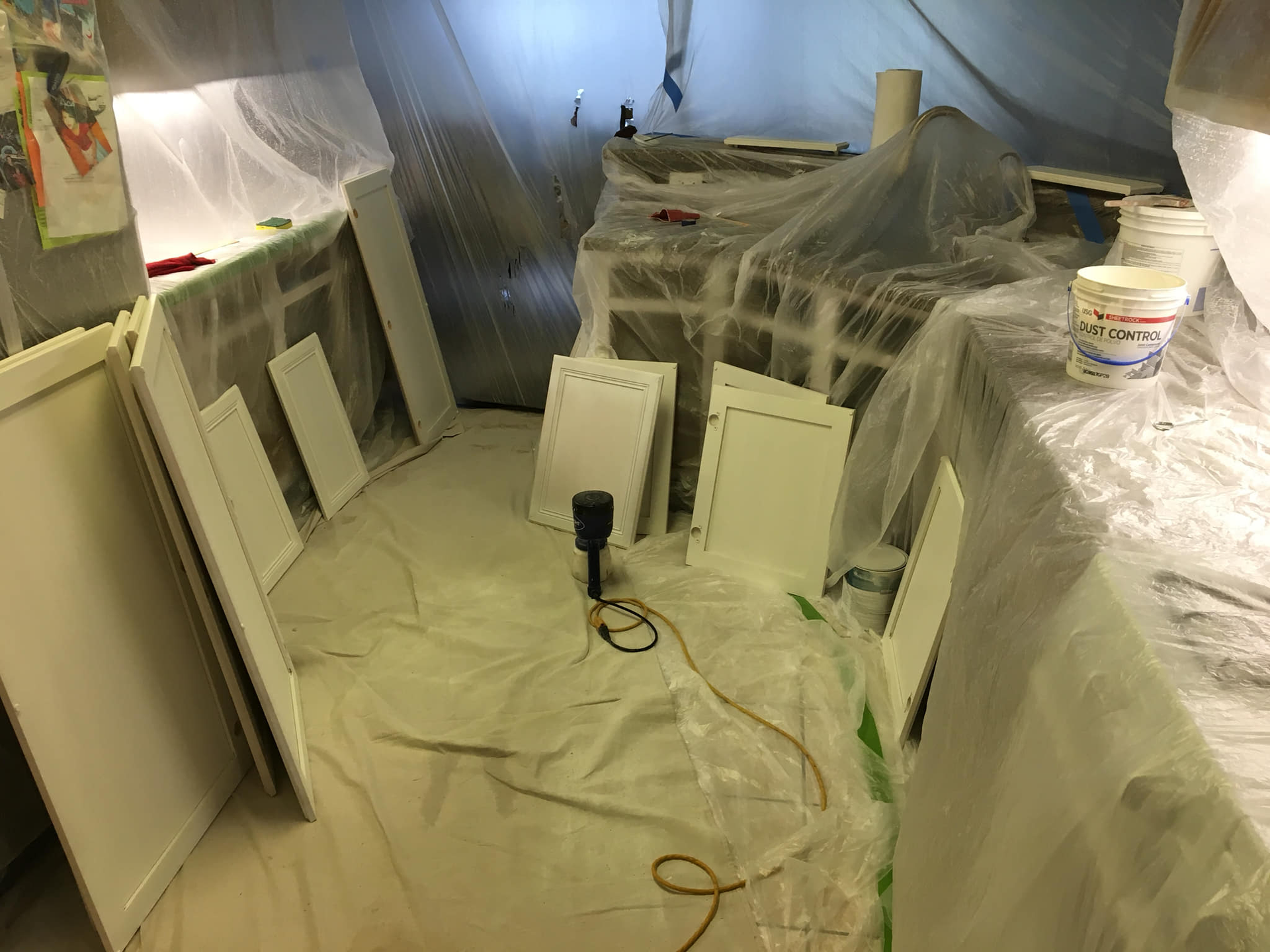 Kitchen cabinets covered in plastic, with painted doors leaning against the wall, ready for installation.