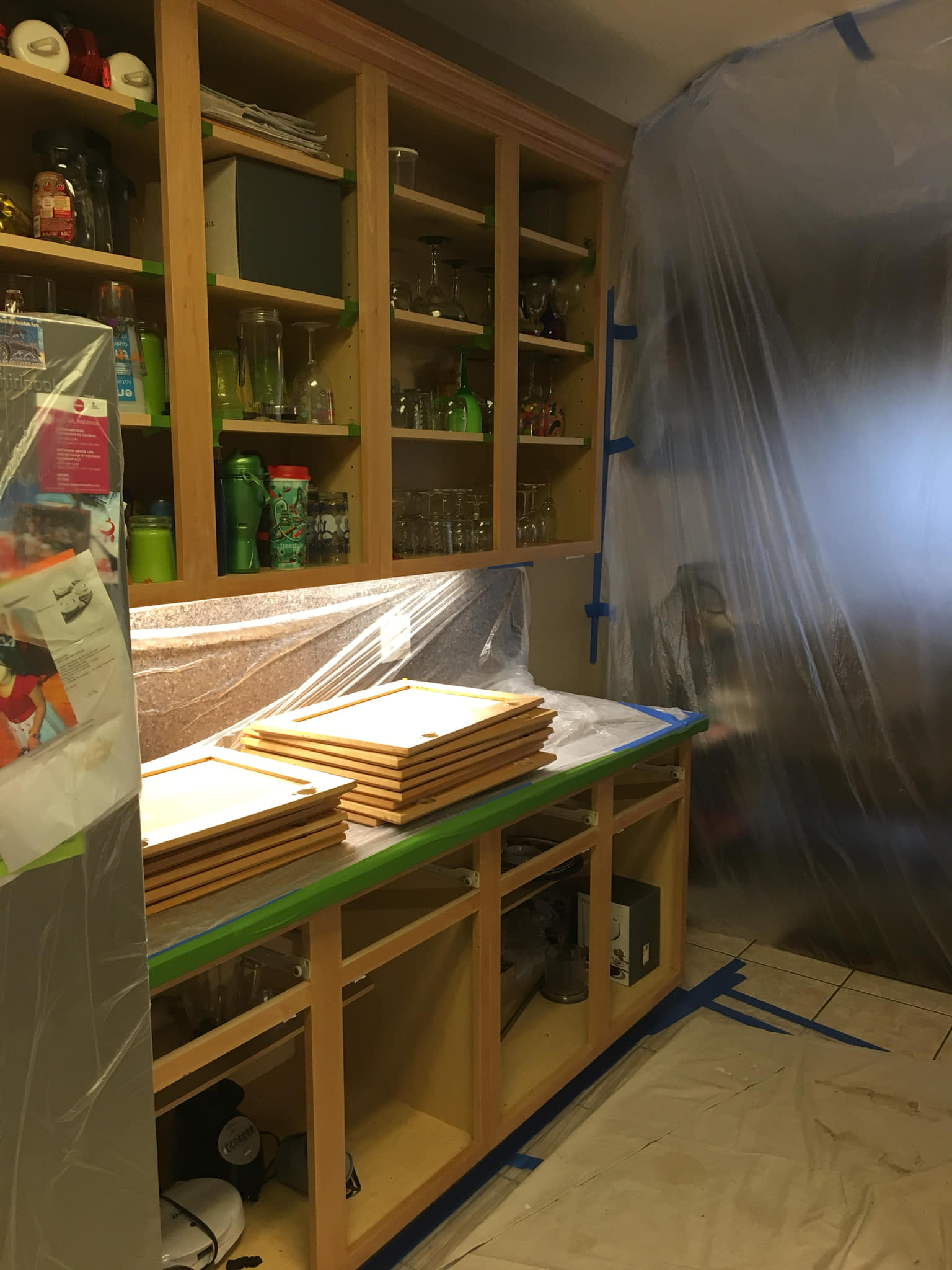 Kitchen with cabinets and countertop partially covered in plastic for renovation.
