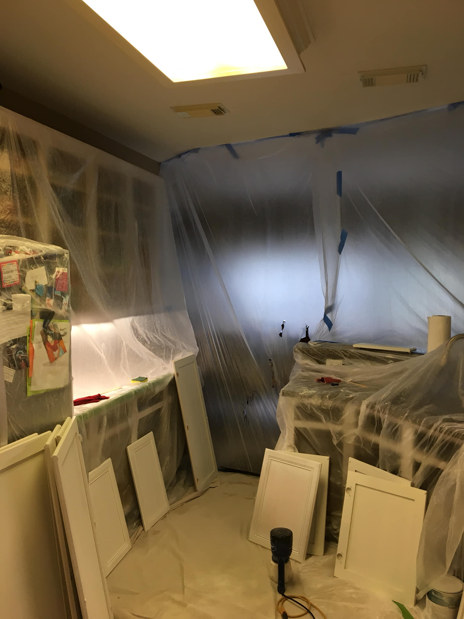 Kitchen cabinets and parts protected with plastic sheeting for painting.