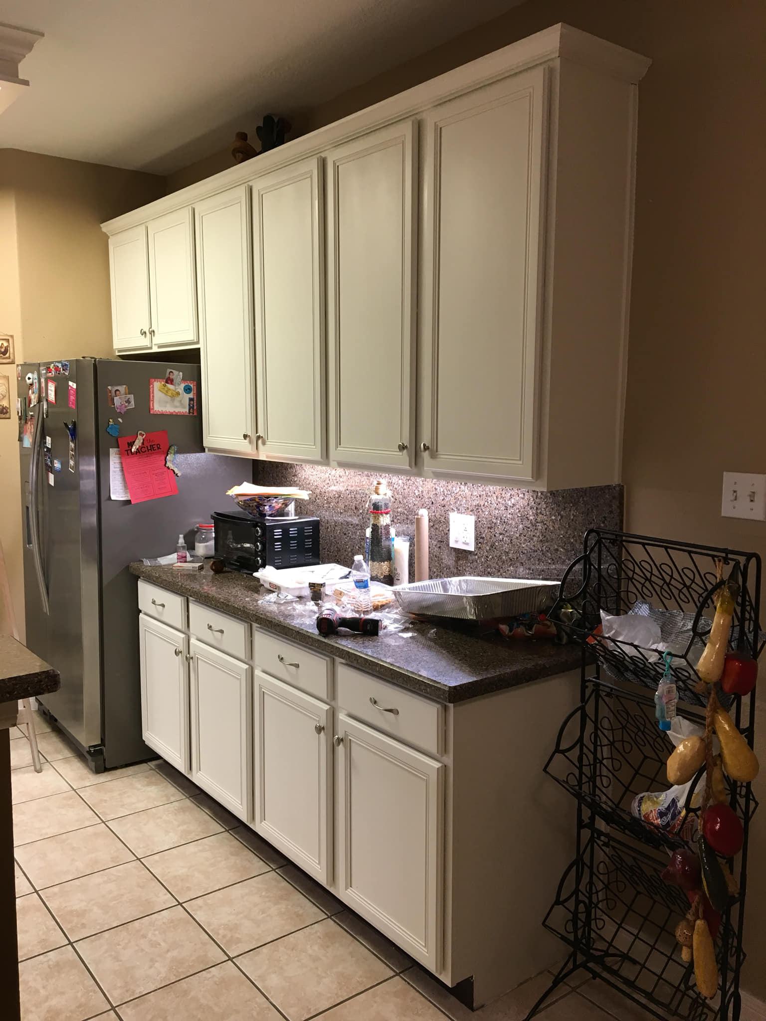 Kitchen with white cabinets, stainless steel refrigerator, and countertop with various items.