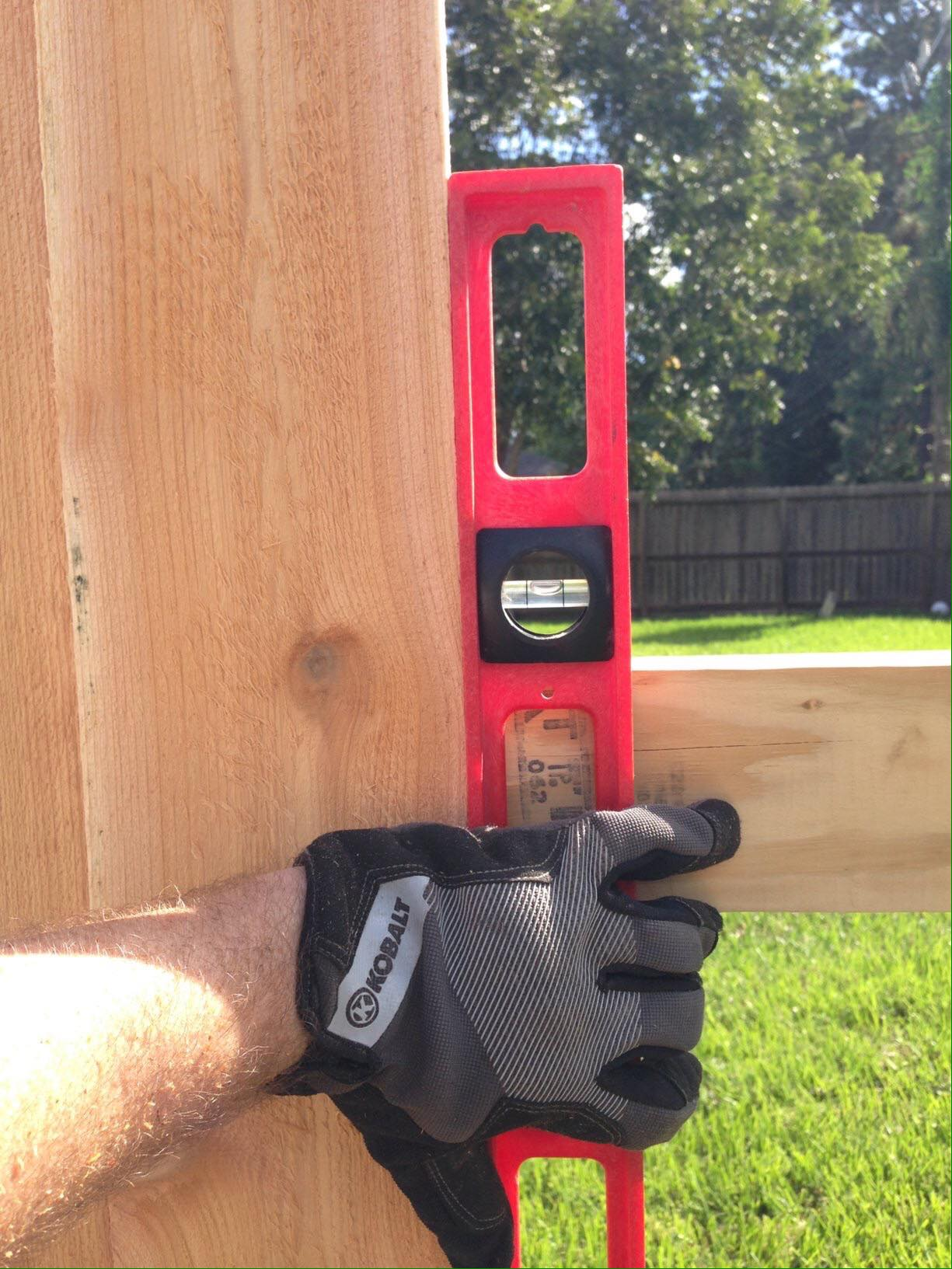 Person using a red level tool on wood structure outdoors, checking for vertical alignment.