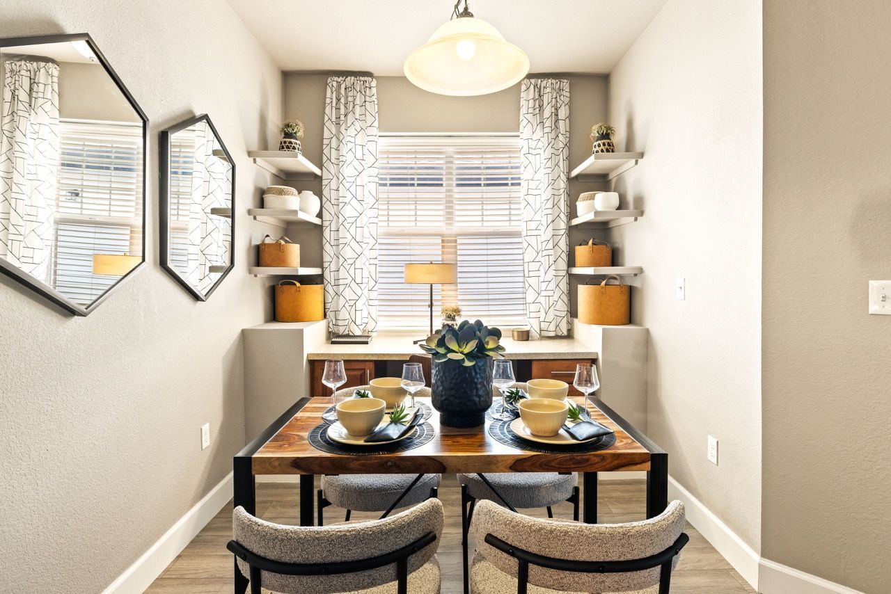 Dining nook in an apartment with a wooden table set for four, centered by a window and shelves.