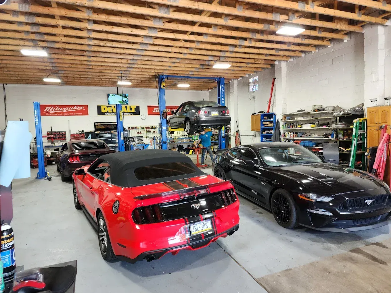 Cars in a garage, one on a lift, a red convertible and a black car in front.