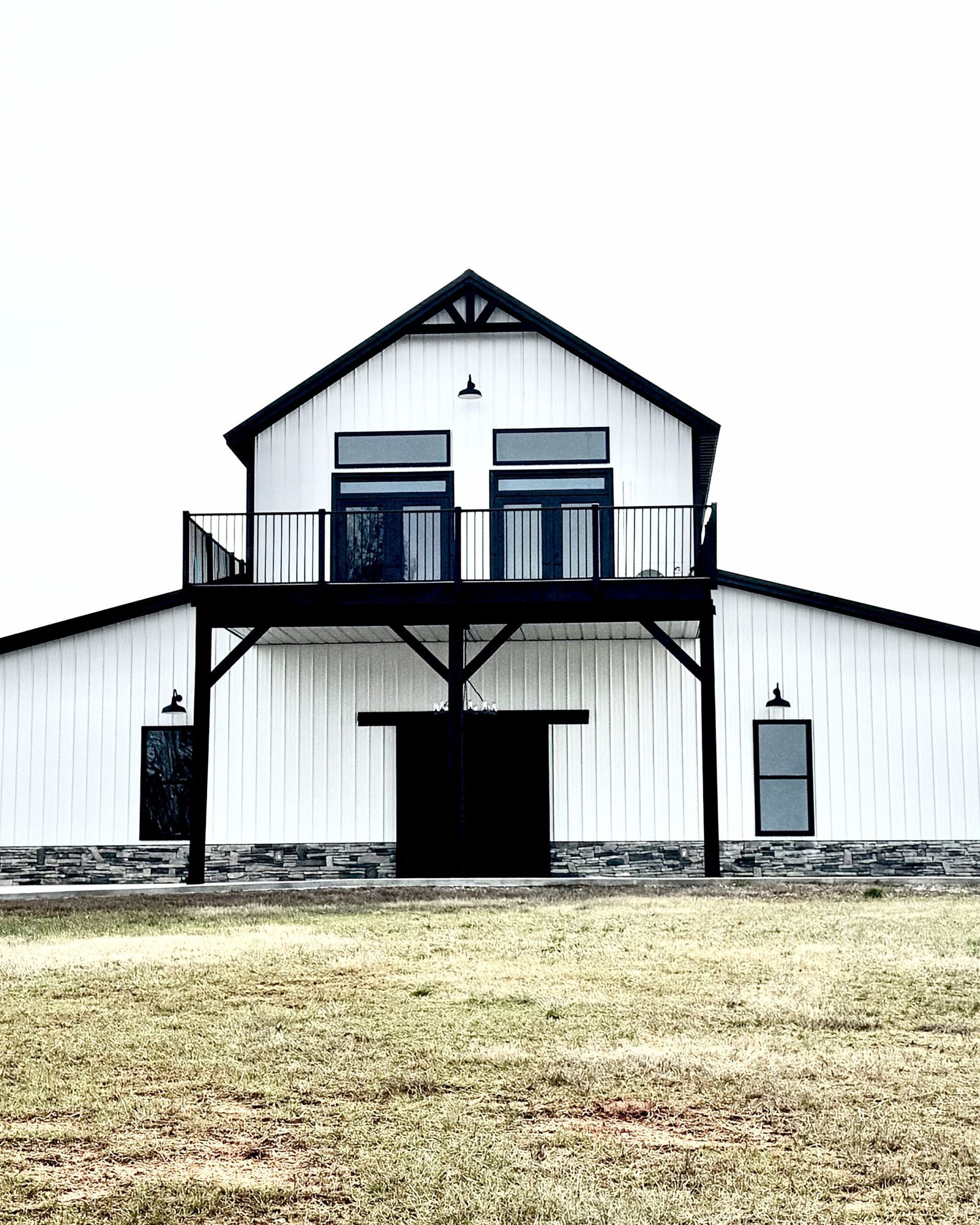 White barn with black trim, balcony, and dark doors under an overcast sky.