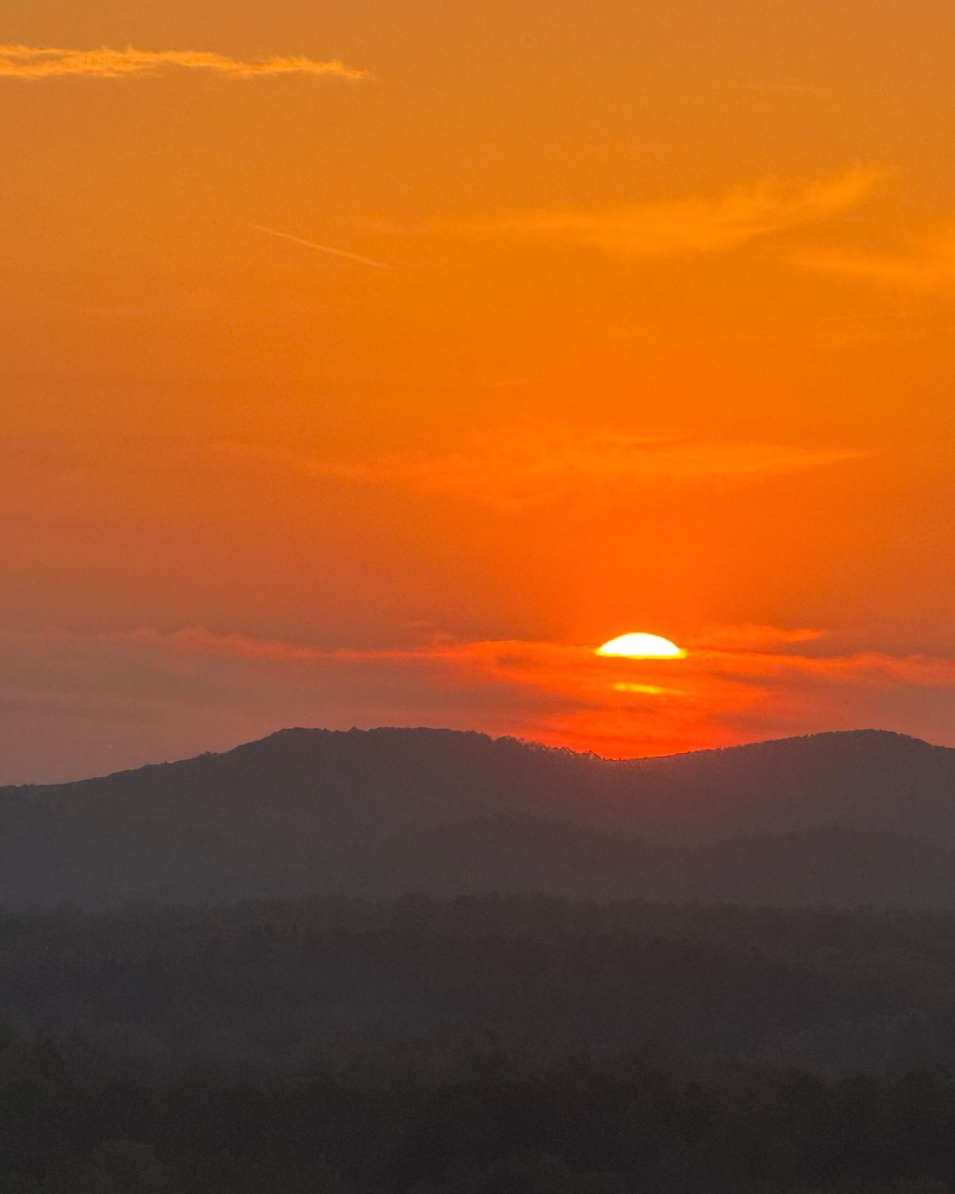 Sunset over silhouetted mountains, bright orange and yellow sky.