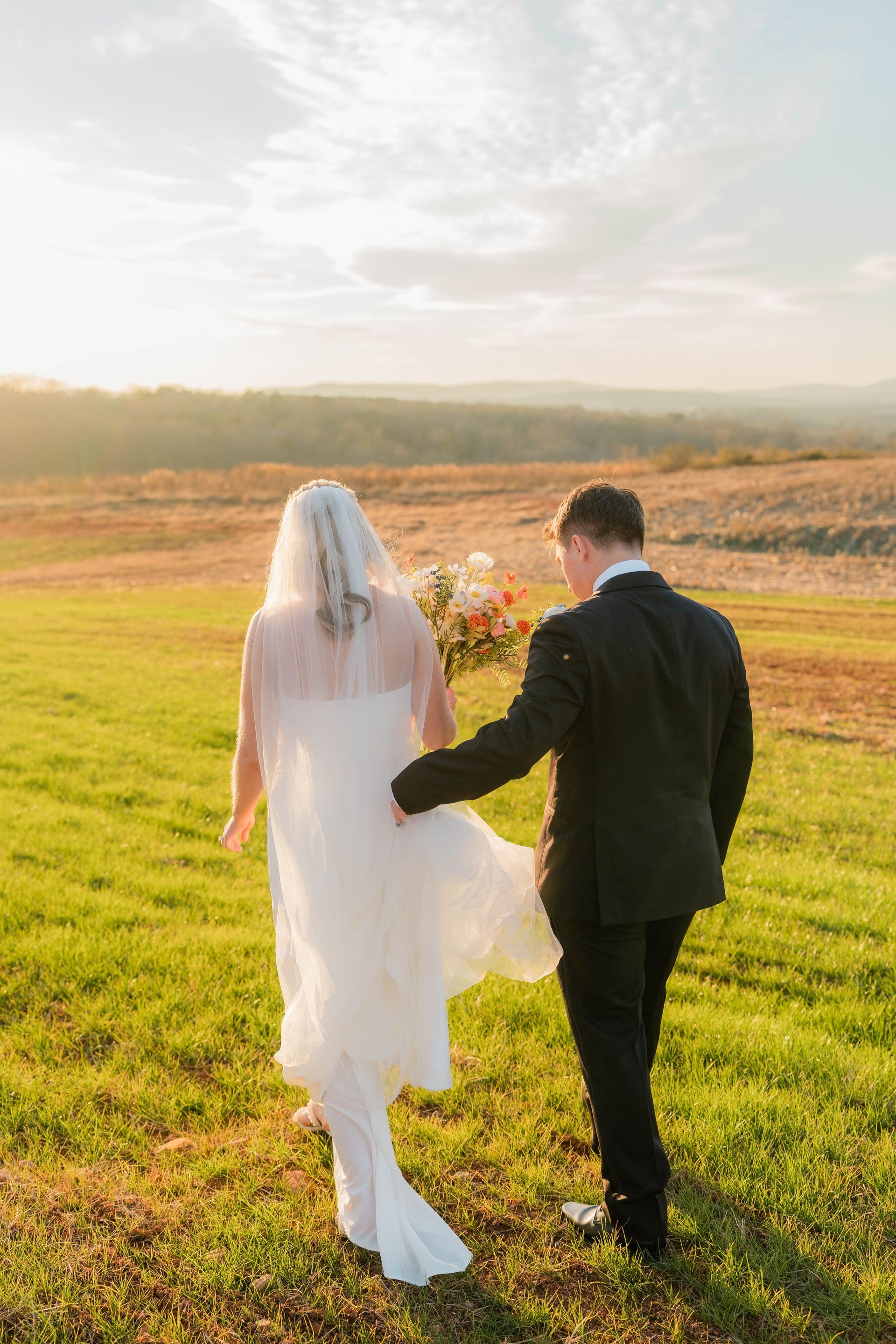 Man pouring champagne for a smiling woman in a wedding dress outdoors.