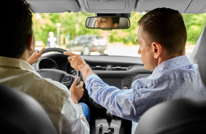 An instructor giving directions during a driving lesson inside a car, pointing toward the road ahead An instructor giving directions during a driving lesson inside a car, pointing toward the road ahead