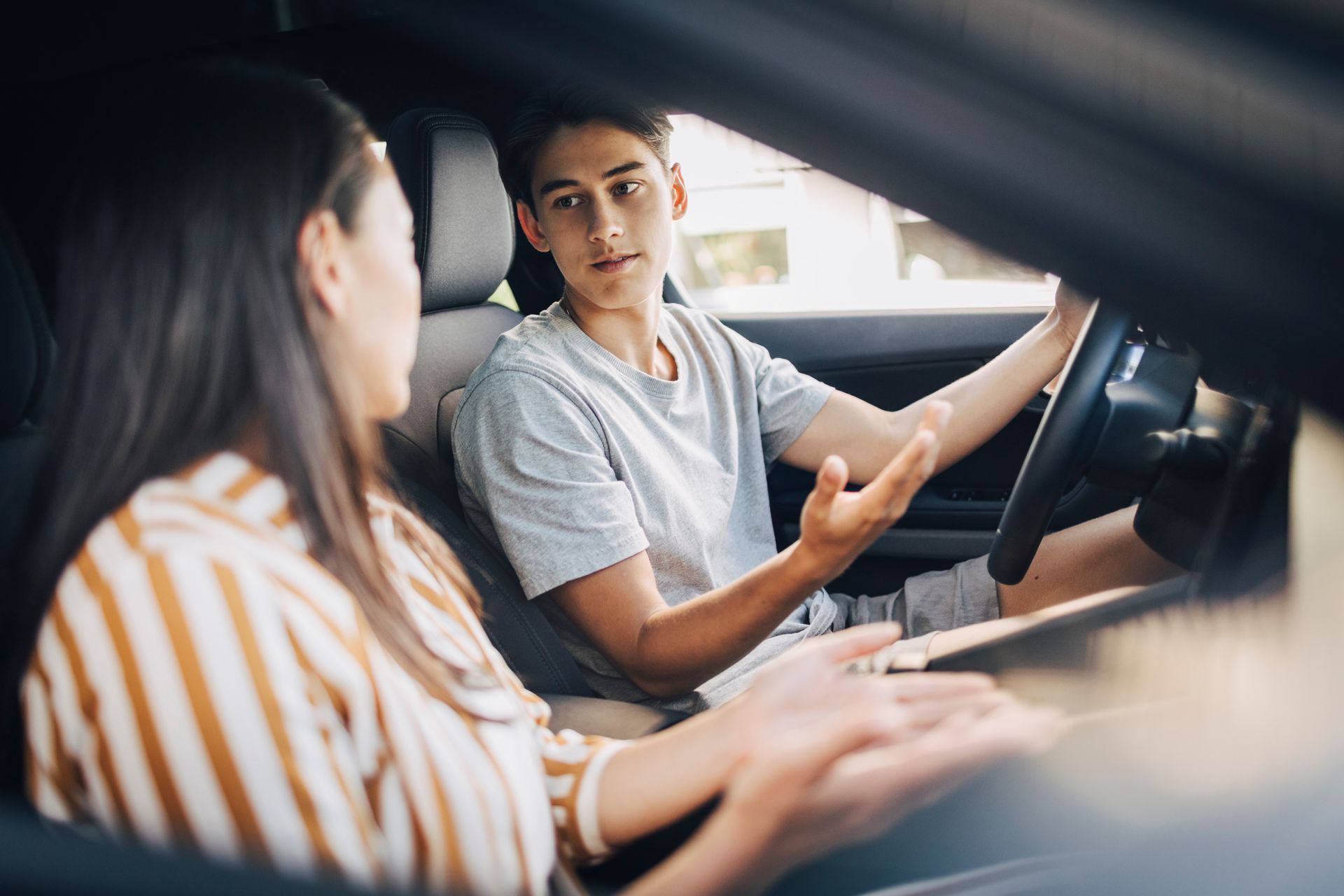 Young man getting driving instructions from a female while sitting in a car.